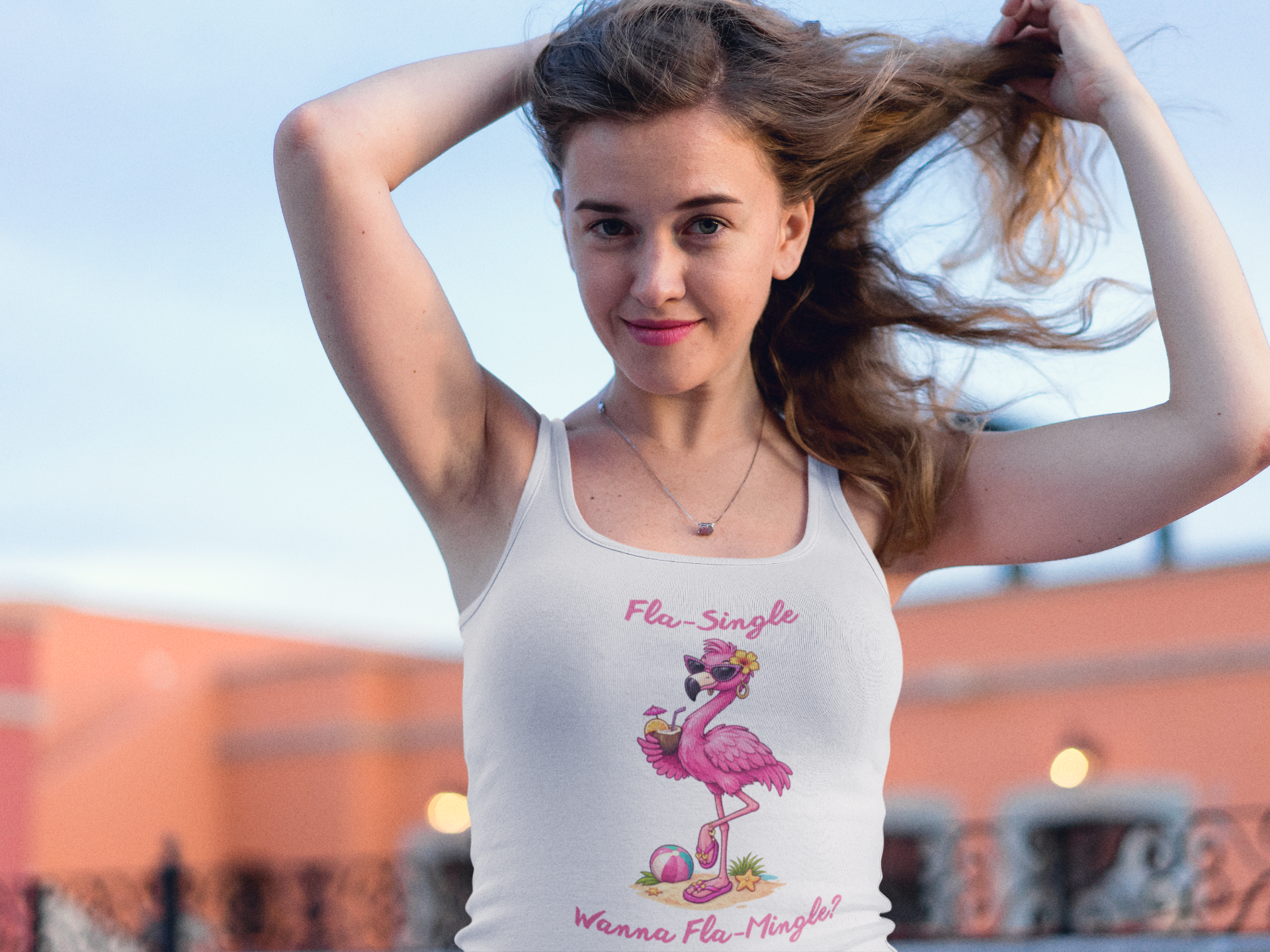 Woman wearing a white tank top with a flamingo design and text, standing outdoors.