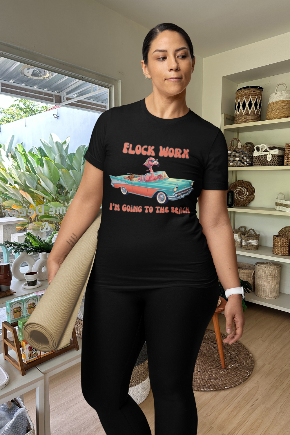 Person wearing a black t-shirt with a graphic design, standing in a room with shelves and plants.