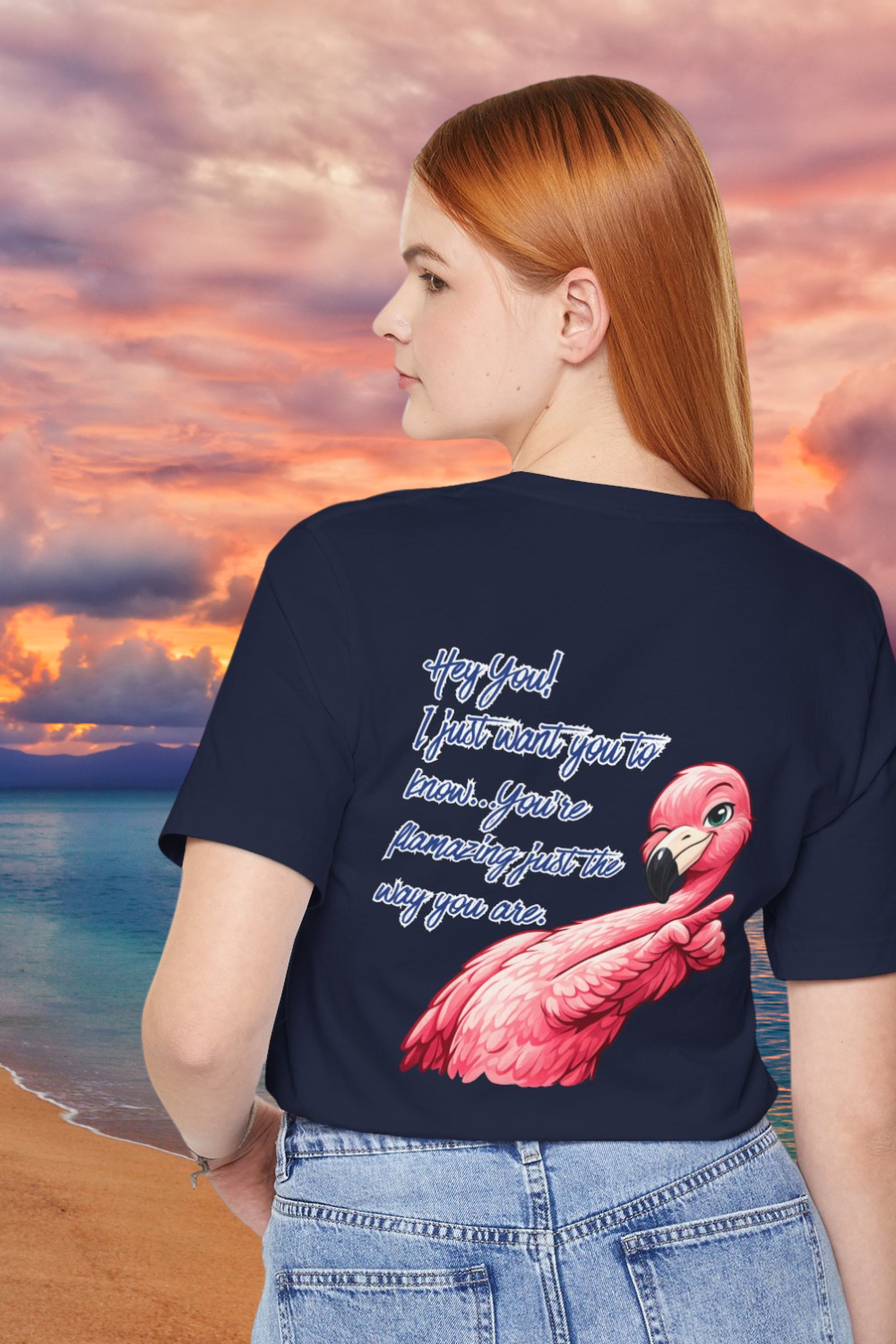 Person wearing a navy blue t-shirt with a pink flamingo design and text, standing against a sunset beach backdrop.